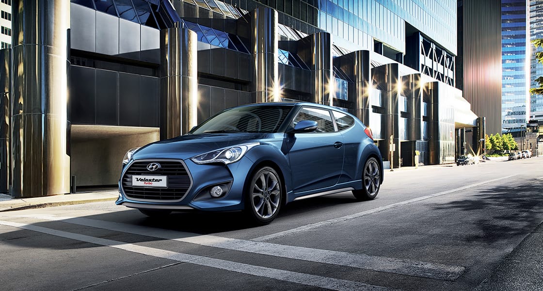 Left side front view of navy Veloster Turbo parked in front of the building