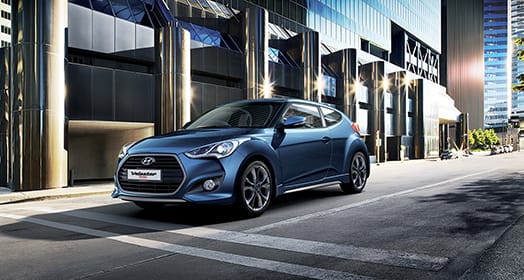 Left side front view of navy Veloster Turbo parked in front of the building