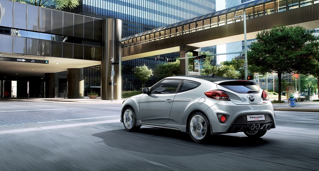 Left side rear view of silver Veloster Turbo parked under the building to building pedestrian bridge