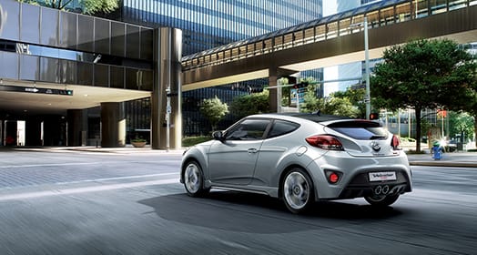 Left side rear view of silver Veloster Turbo parked under the building to building pedestrian bridge