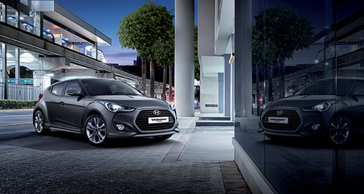 Side front view of dark gray veloster Turbo parked in front of the building with reflection on the wall