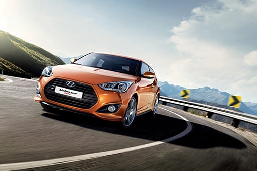 Front view of tangerine orange Veloster Turbo driving on the road