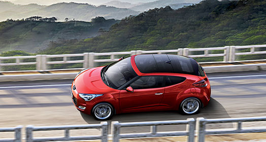 Sky view of driving red Veloster from left side viewpoint