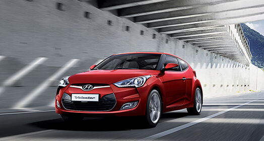 Left side front view of red Veloster driving on the road