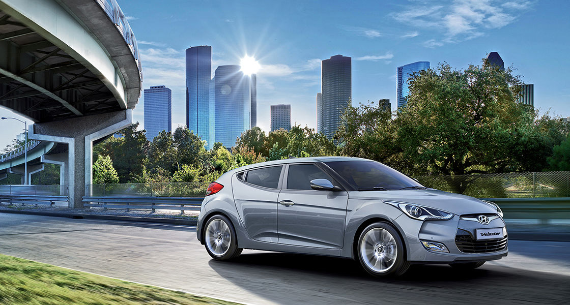 Side view of silver Veloster driving with the city background