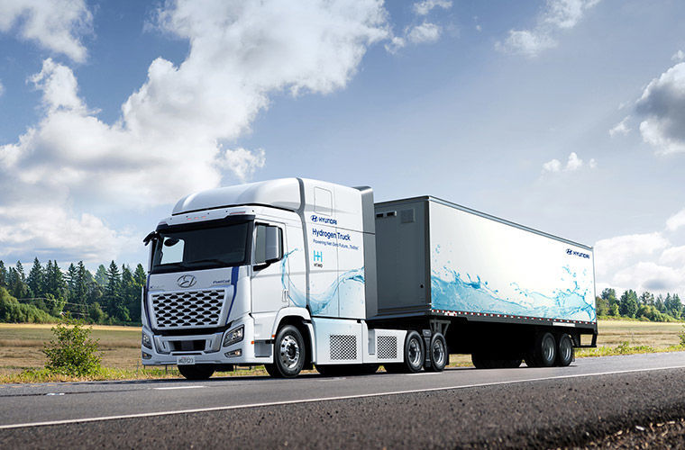 A white Hyundai XCIENT fuel cell truck driving along the road with the words XCIENT Fuel Cell on the side.