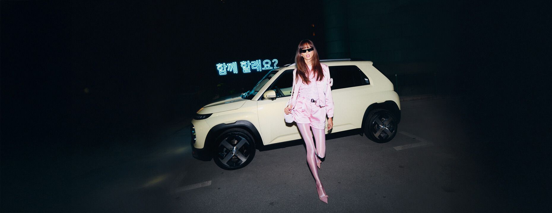 Park halinde yeni Hyundai INSTER küçük elektrikli otomobilden uzaklaşan pembe kıyafetli bir kadın.