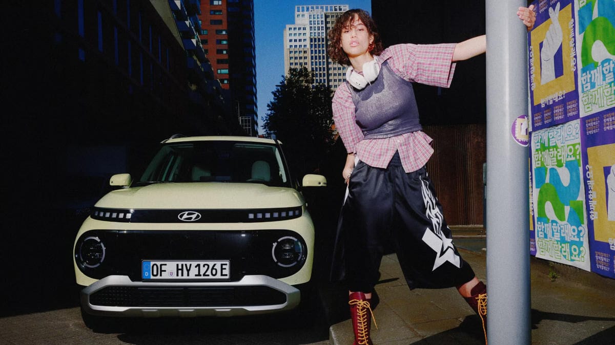 Yol kenarında park halinde yeni Hyundai INSTER küçük elektrikli otomobilden uzaklaşan bir kadın.