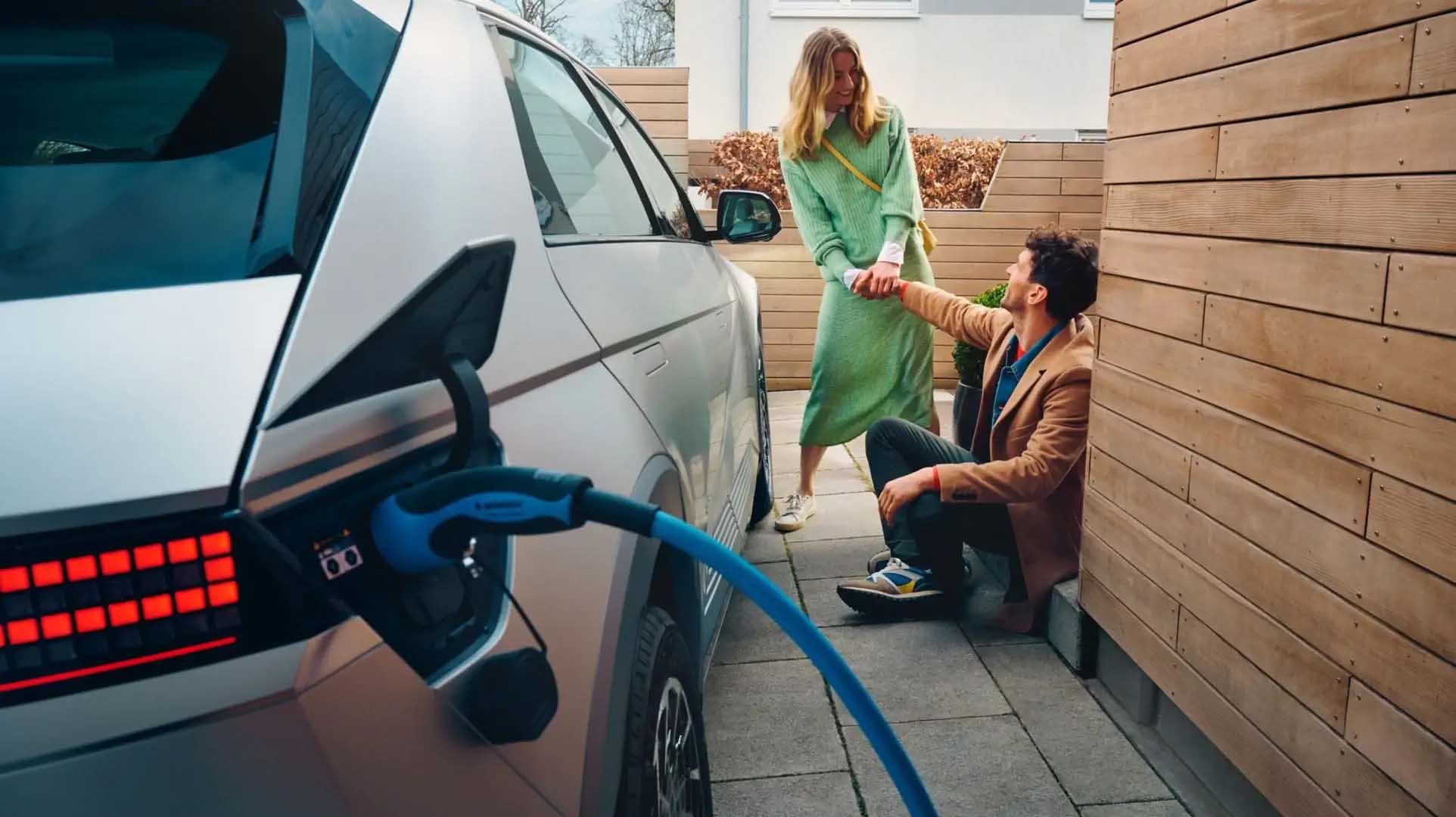 The Hyundai IONIQ 5 electric midsize CUV charging at home, a young couple sitting next to it.