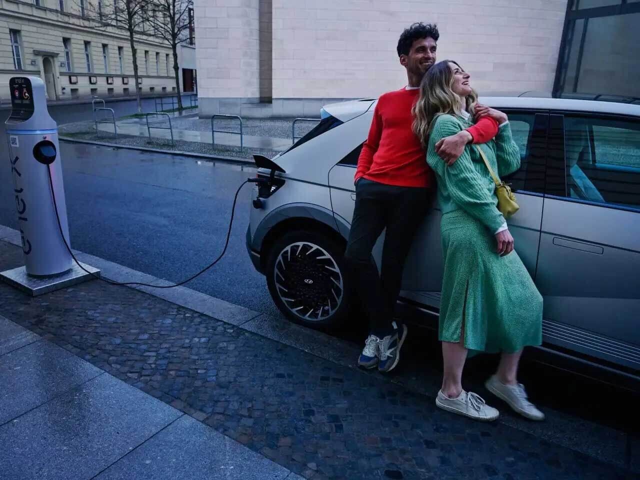 A  man and a woman hugging next to the Hyundai IONIQ 5 which is plugged in for charging.