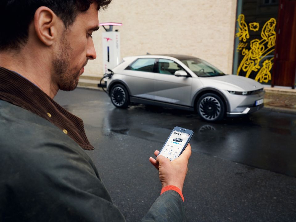 A man checking his Hyundai app while charging the Hyundai IONIQ 5 at an IONITY charging station.