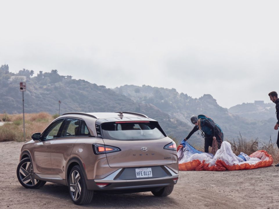 Two paragliders packing their chutes next to a Hyundai NEXO hydrogen fuel cell vehicle.