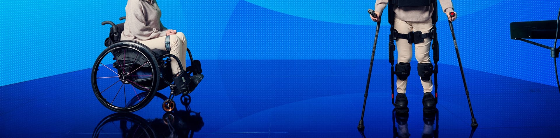 A photo of a woman in a wheelchair facing another woman standing while wearing the medical exoskeleton X-ble MEX