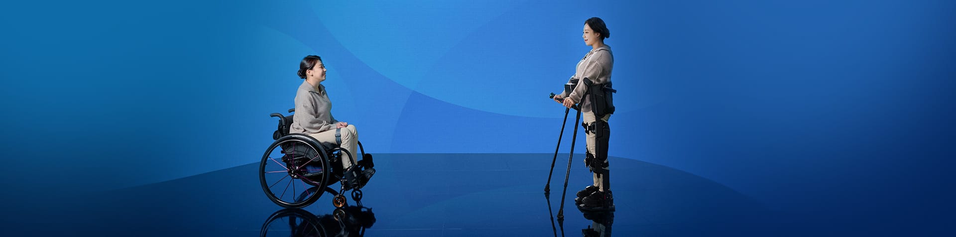 A photo of a woman in a wheelchair facing another woman standing while wearing the medical exoskeleton X-ble MEX