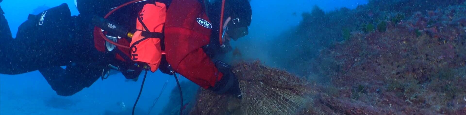 Three submerged scuba divers bringing a ghost net up from deep blue waters.