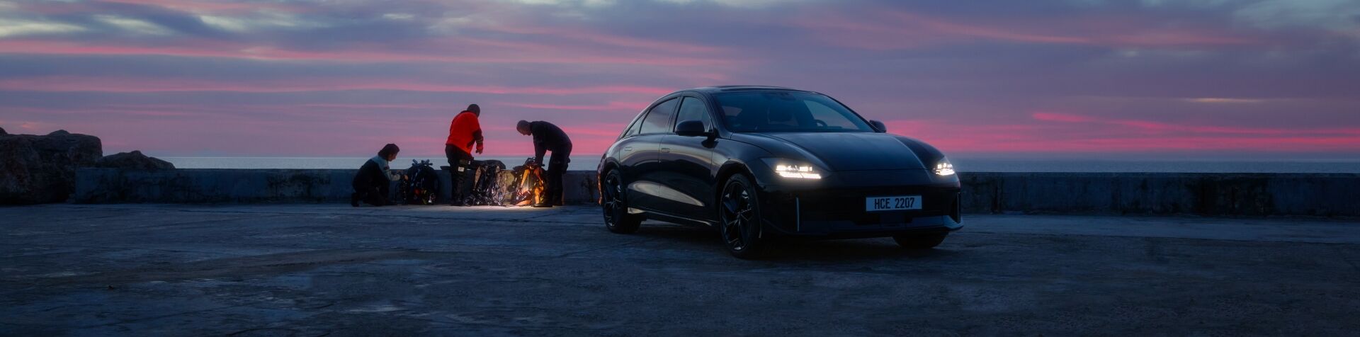 A Hyundai IONIQ 6 is parked at the beach with people in the background sorting through material.