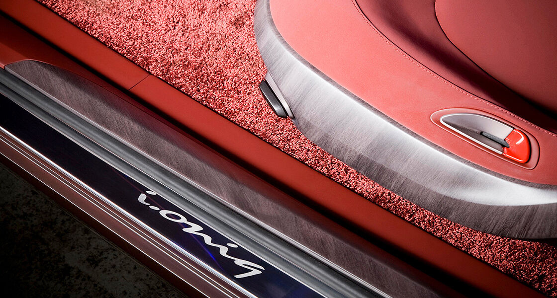 Extreme close-up view of i-oniq at the silver finished threshold with its name engraved and the front cabin seat and carpet in red color next to it