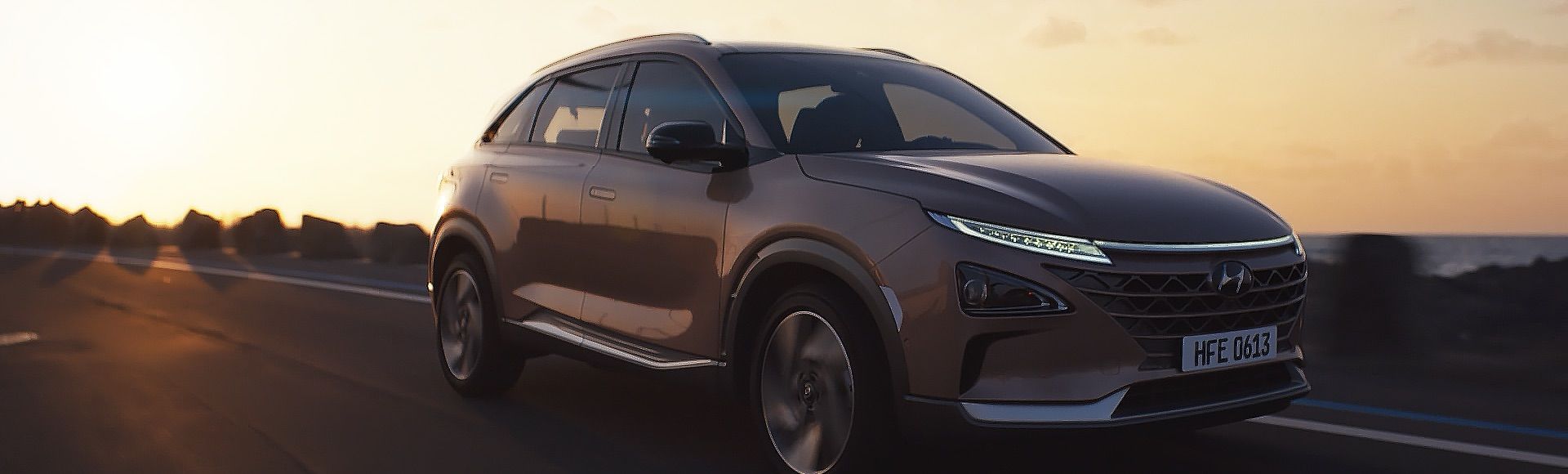 A copper colored Hydrogen NEXO car drives along a road at sunset.