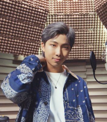 BTS member RM standing in a recording studio wearing a blue paisley jacket and a white t-shirt.