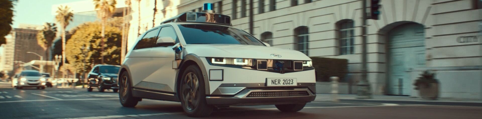 A white Hyundai IONIQ 5-based robotaxi driving along a busy road in LA. 