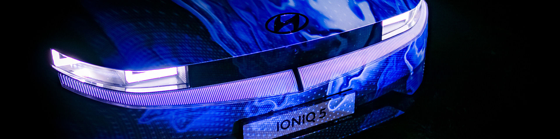 The front of an IONIQ 5 with blue artwork projected onto it.