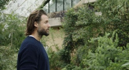 Profile of David de Rothschild standing in a greenhouse surrounded by climbing green plants.