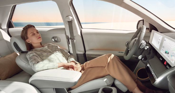 Blond woman sleeping in the reclining front seat of the IONIQ 5. She is wearing plaid jacket and brown pants and the interior furnishings are all cream in color.