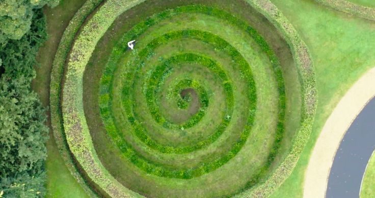 Birds’ eye view of David de Rothschild walking around a green labyrinth pattern.