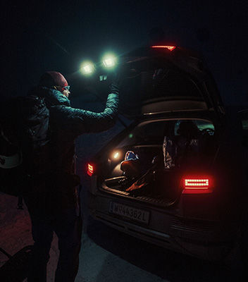 사진 작가 니콜라스 럼멜트가 어둠 속에서 미등과 뒷문에 있는 자동차의 파라메트릭 조명에 비추어 IONIQ 5의 트렁크를 열고 있습니다.