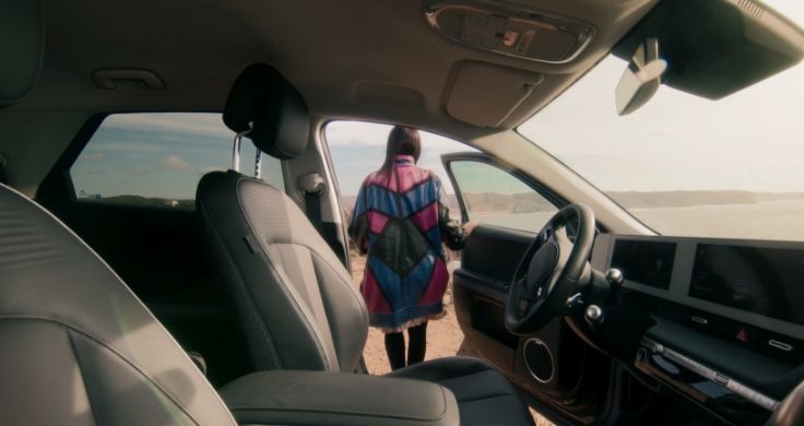 Sofia Kourtesis exiting the IONIQ 5, she is wearing a pink and blue jacket and holding the side door open.