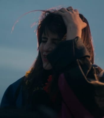 DJ Sofia Kourtesis holding her head and feeling the music. She has brunette hair and is wearing a black jacket.