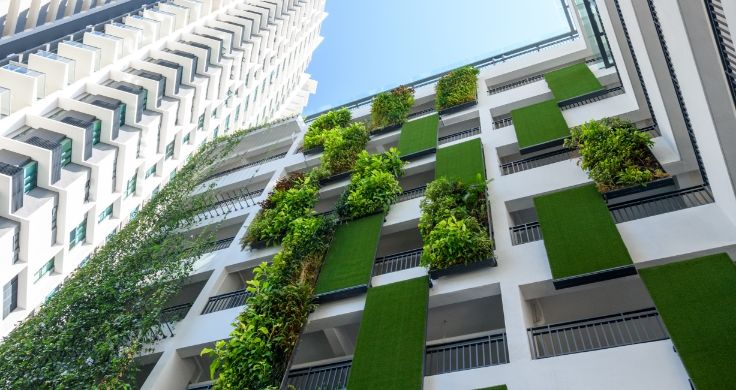 The side of a modern-looking apartment block which has green plants growing up the side of it.