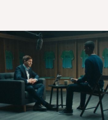 Steven Gerrard sitting in the changing room surrounded by Team Century jerseys, being interviewed.