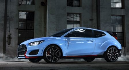 Side view of a blue Hyundai Veloster N driving along a street at night.