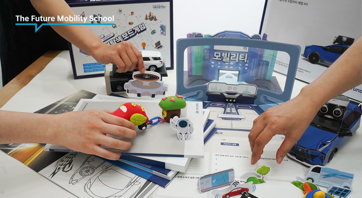 The Future Mobility School Experience Kit is displayed on the table, including the clay building kit, drawing books, workout sheets, and the autonomous driving model car kit