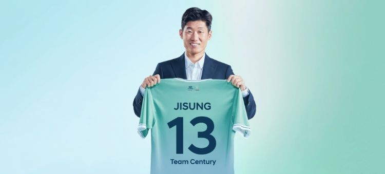 Team Century 멤버 박지성이 뒷면에 파란색으로 숫자 13이 새겨진 녹색 Team Century 티셔츠를 들고 카메라를 향해 웃고 있다.