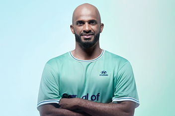 A portrait of smiling male football player and Team Century member Ali Al-Habsi in front of a blue and green background.