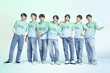 All 7 BTS members standing in a line facing forward. Each member has a green and gray Team Century shirt on with the Hyundai logo and Goal of the Century emblazoned in dark blue across the front.