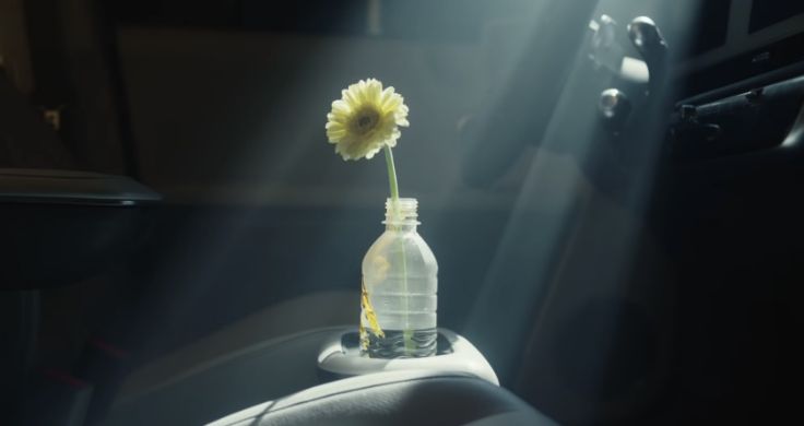 A plastic bottle with a single yellow flower in it sitting in the cup holder in an Hyundai IONIQ 5 with light pouring onto it. 