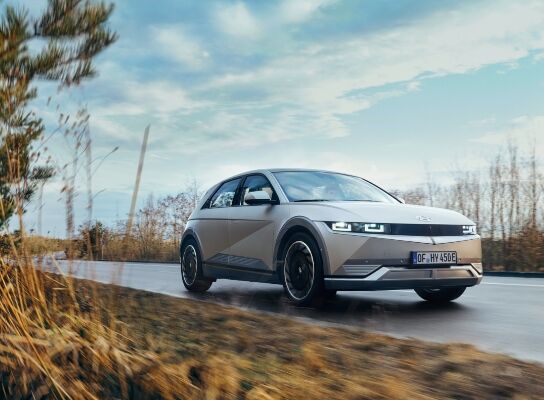 A gray Hyundai IONIQ 5 driving along a road surrounded by nature.