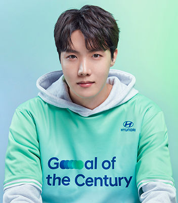 BTS member J-Hope wearing a green Team Century shirt with a gray hoodie underneath.
