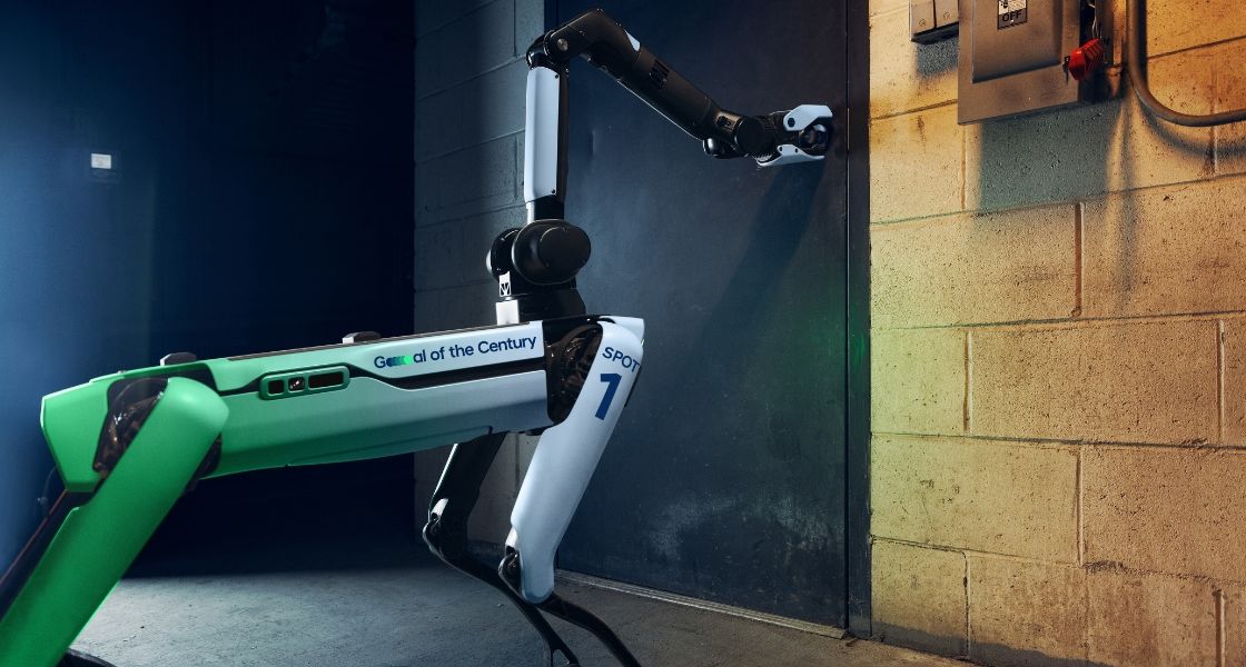 The Spot robot using its arm to open a heavy metal door. 
