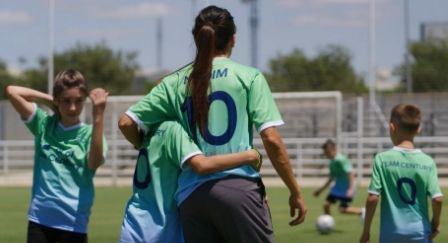 Football player Nadia Nadim wearing her green and blue Team Century jersey balancing a football on her head in front of a blue and green background.