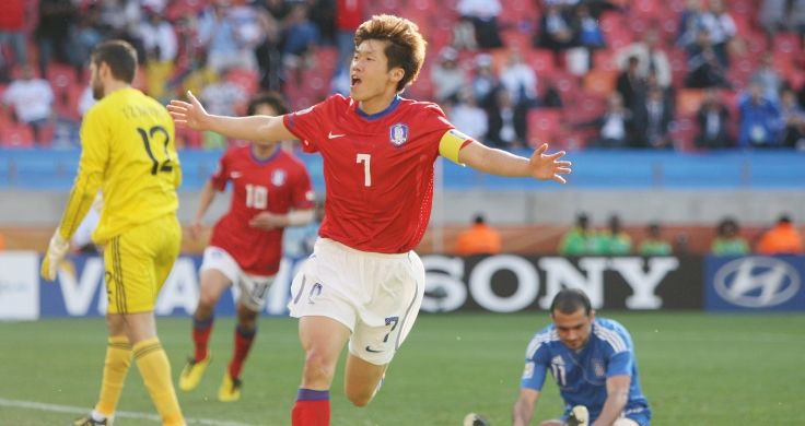 Team Century male footballer Jisung Park running victoriously on the pitch with arms extended while wearing South Korea’s red jersey and captain’s armband.