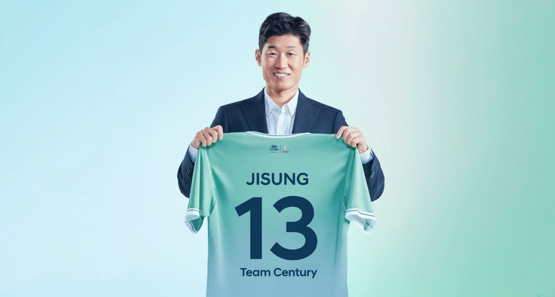 Team Century 멤버 박지성이 뒷면에 파란색으로 숫자 13이 새겨진 녹색 Team Century 티셔츠를 들고 카메라를 향해 웃고 있다.