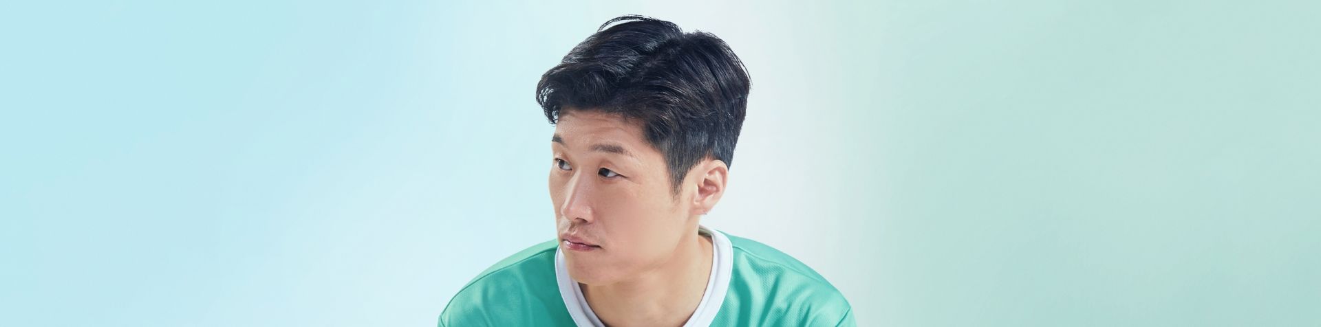 A portrait of male football player and Team Century member Jisung Park looking to his right in front of a blue and green background.