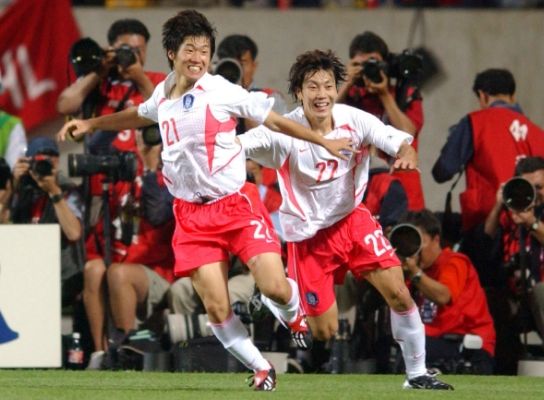 Team Century 멤버 축구선수 박지성이 등번호 21번이 새겨진 2002년 한국 원정경기 흰색 유니폼을 입고 같은 팀 동료와 함께 경기장을 달리고 있다.