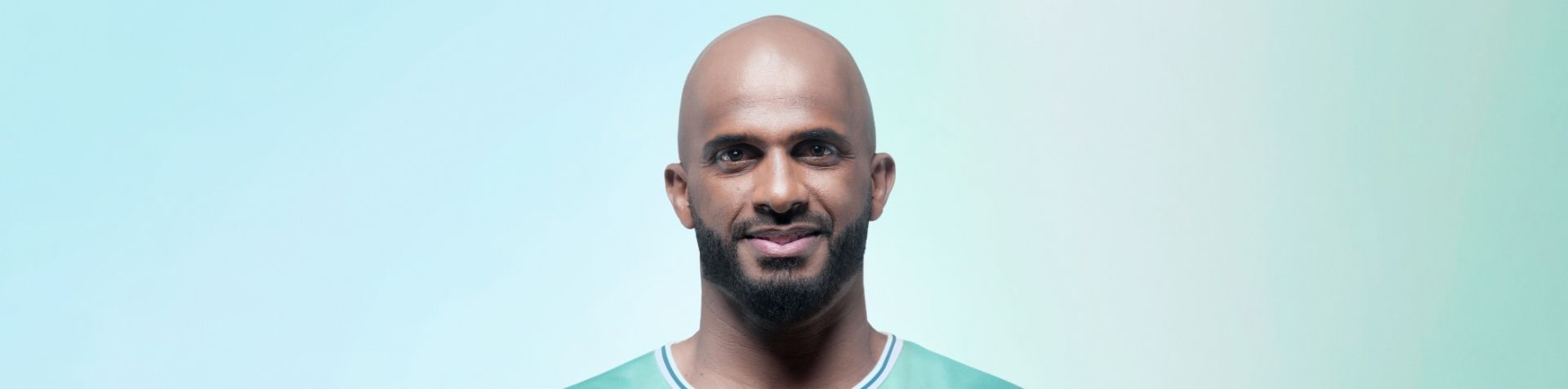 A portrait of smiling male football player and Team Century member Ali Al-Habsi in front of a blue and green background.