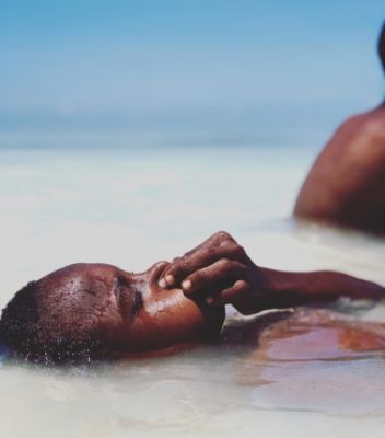 One of Nicky’s photographs depicting a child submerged in the shallow ocean holding their nose with another unseen person sat behind them.