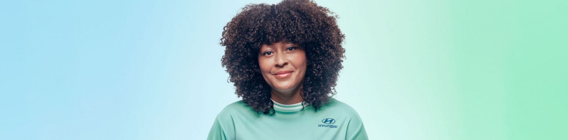 A close-up of Nicky Woo’s head and shoulders. Her hair is curly, and she is wearing a light green Team Century jersey with the Hyundai logo on it.
